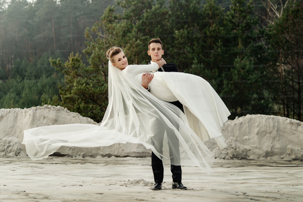 stylish groom picking up his gorgeous bride at sandy beach lake, true emotions, luxury wedding