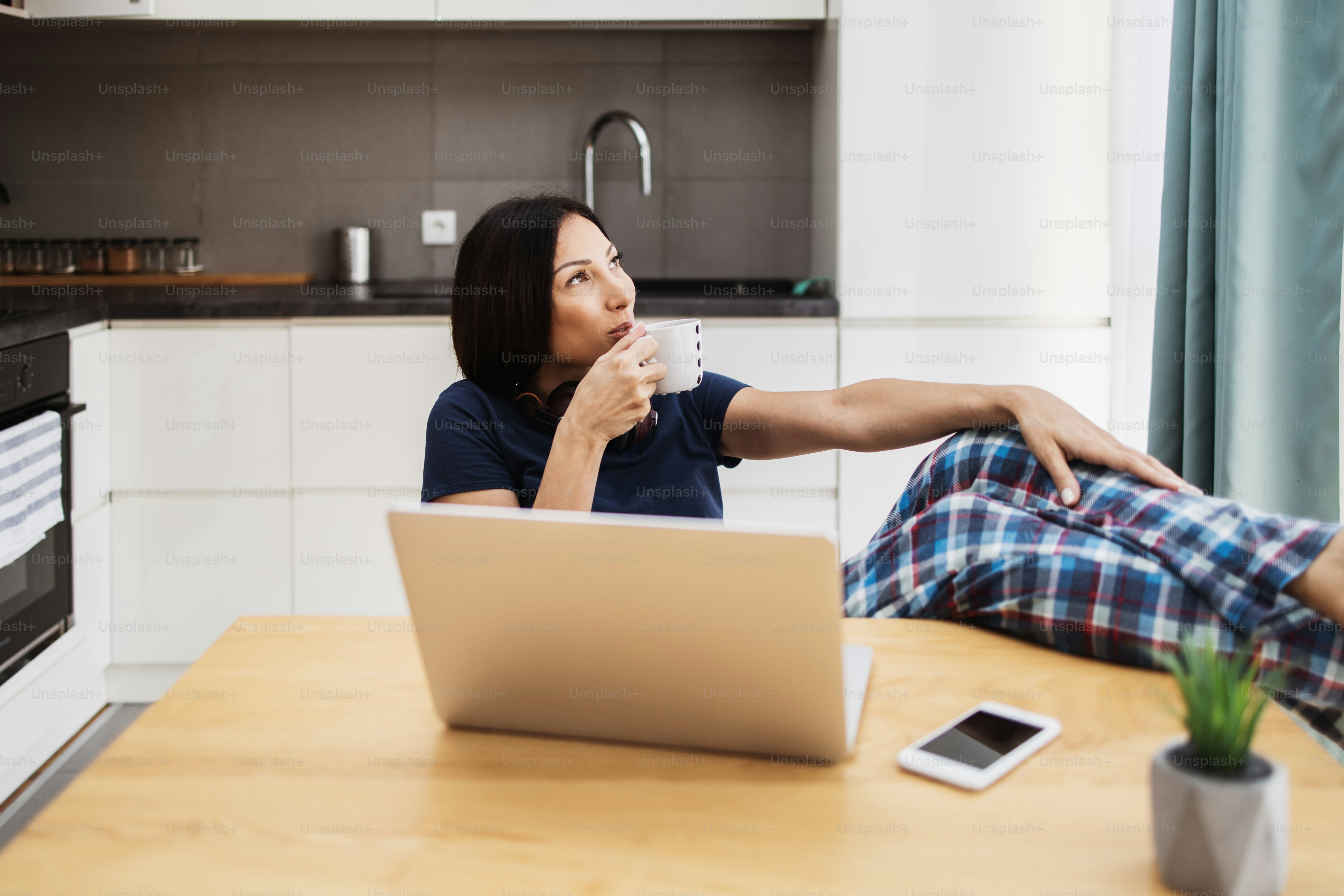 Attractive and happy middle age female freelancer is working and smiling at her home. Modern kitchen in background. Freelancing job concept.