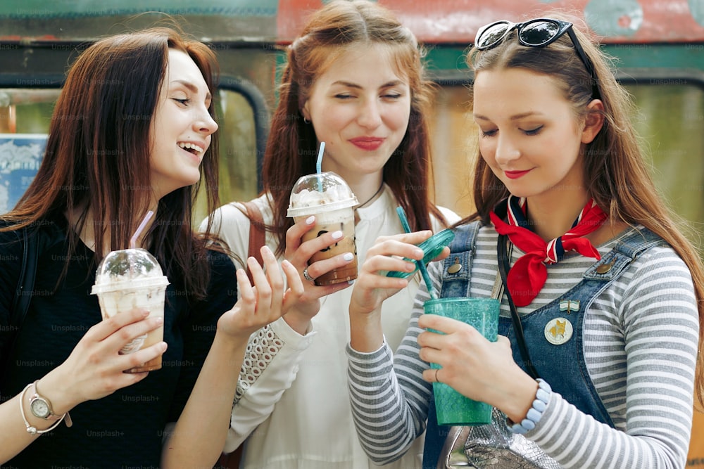 Stilvolle glückliche Gruppe von Frauen, die Eis und Cocktails in den Händen halten und Spaß haben, sich in der City Street entspannen, freudige Momente