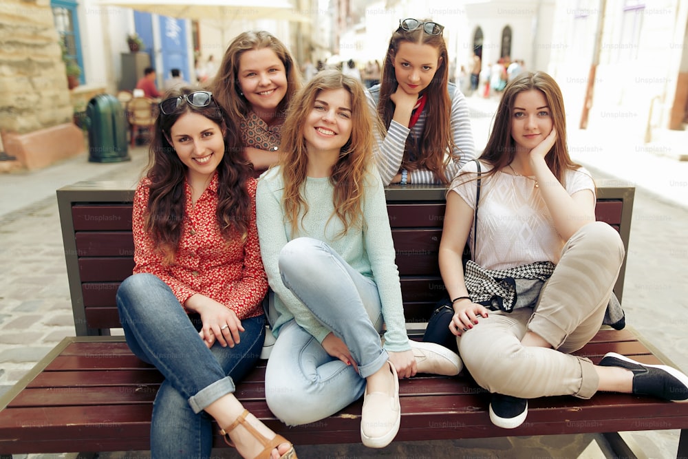 Mujeres felices con estilo hipsters vestidos de moda sonriendo y sentados en el banco en la calle de la ciudad de Europa, concepto de amistad de momentos alegres