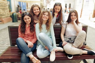 stylish happy women hipsters fashionable dressed smiling and sitting on bench in europe city street, joyful moments friendship concept