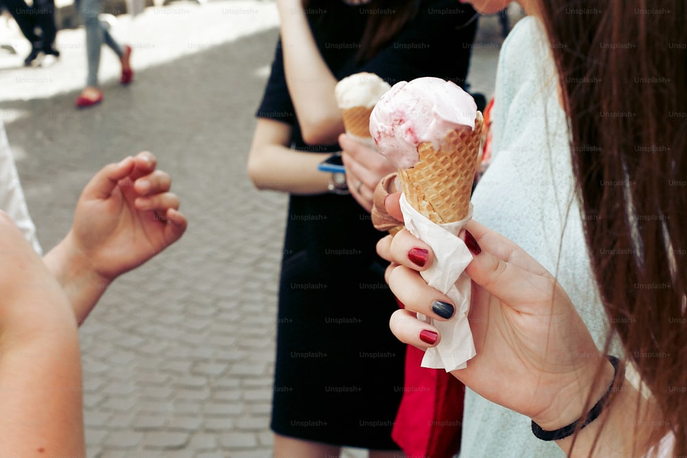 Helado en mano. Grupo de mujeres que sostienen chocolate y helado rosa en las manos de cerca, festejando y divirtiéndose en la calle de la ciudad'