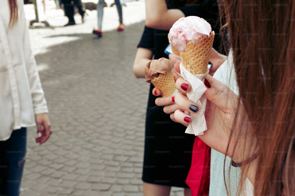 Eis in der Hand. Gruppe von Frauen, die Schokolade und rosa Eis in den Händen halten, feiern und Spaß haben in der Stadtstraße