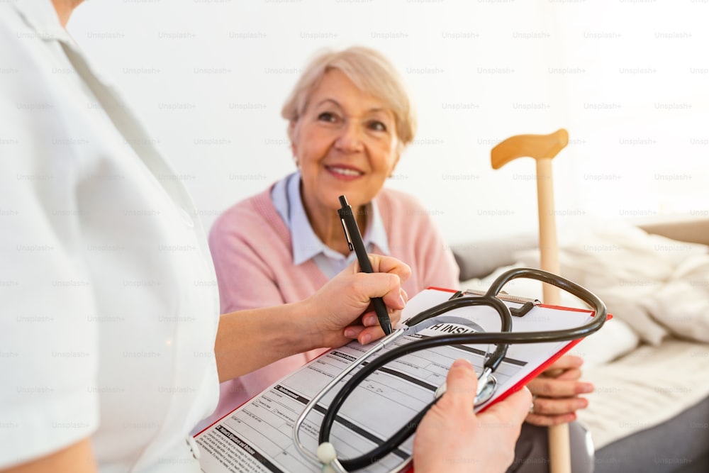 Senior woman is visited by her doctor or caregiver. Female doctor or nurse talking with senior patient. Medicine, age, health care and home care concept. Senior woman with her caregiver at home