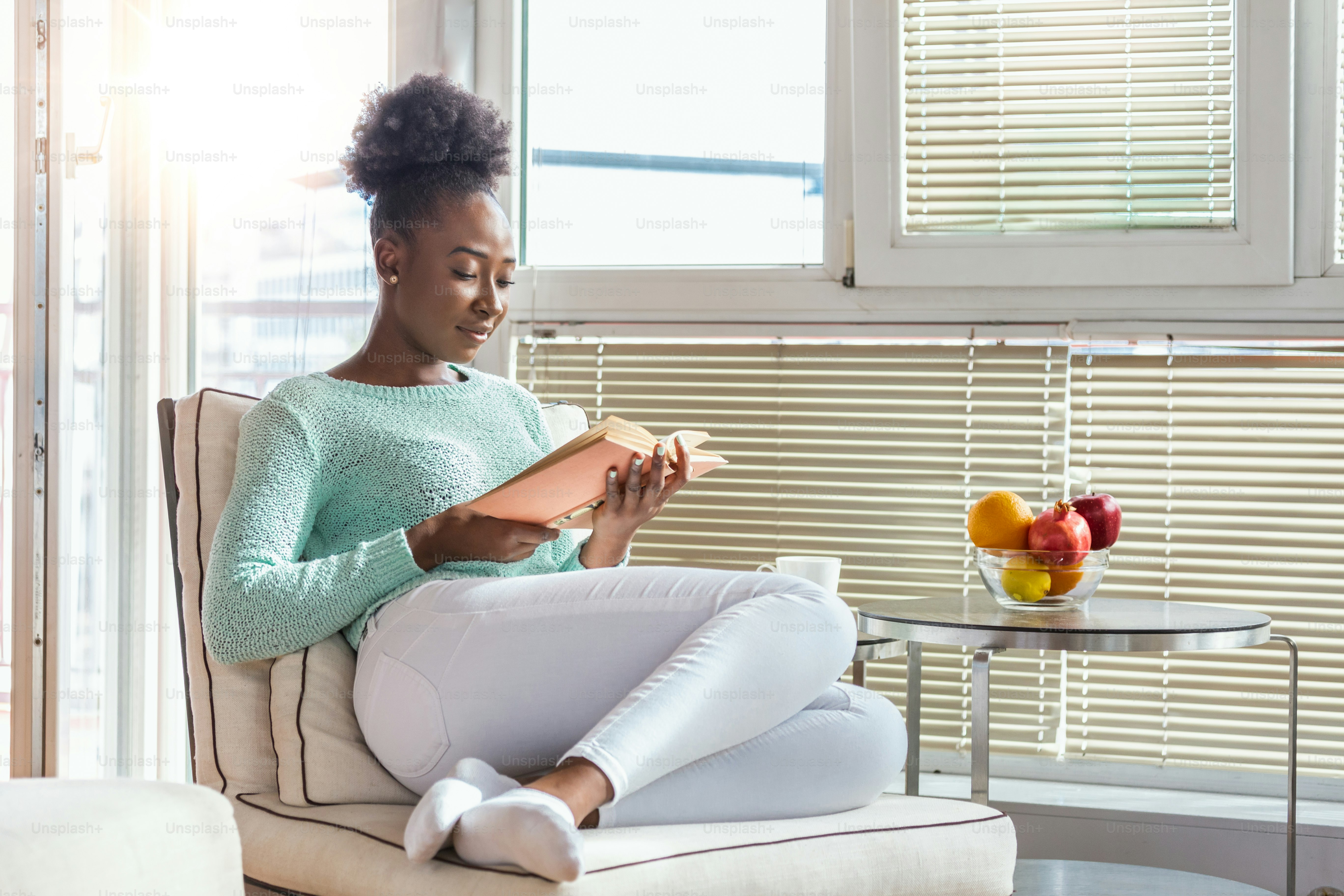 Cozy sofa and a beautiful girl, reading a book, concepts of home and comfort, place for text. Beautiful young black woman reading book near window at home. Stay home