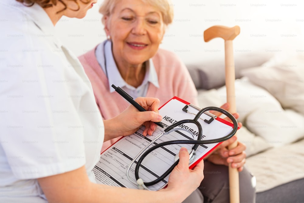 Senior woman is visited by her doctor or caregiver. Female doctor or nurse talking with senior patient. Medicine, age, health care and home care concept. Senior woman with her caregiver at home