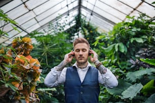 Hombre joven con auriculares de pie en invernadero en jardín botánico. Concepto de negocio verde.