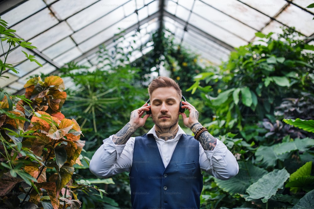 Junger Mann mit Kopfhörern steht im Gewächshaus im Botanischen Garten. Green Businessness-Konzept.