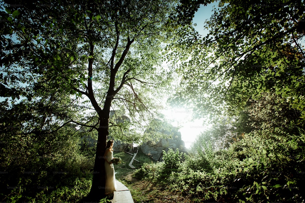 stylish bohemian bride standing in light in the sunny woods