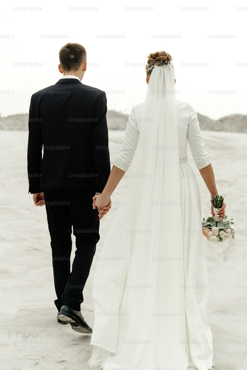 hermosa novia y novio caminando tomados de la mano y mirándose el uno al otro en el lago de arena de la playa, verdaderas emociones