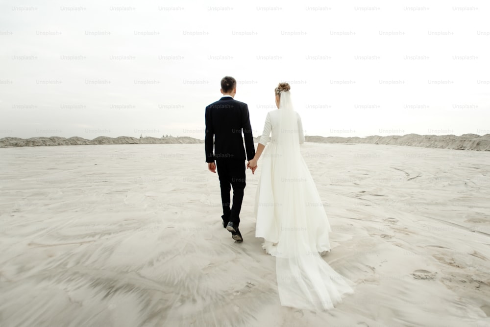 gorgeous bride and groom walking holding hands and looking ar each other at sandy beach lake, true emotions