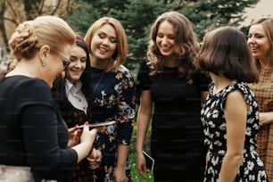 stylish elegant women holding and showing phone screen at celebration sunny in park, funny moment