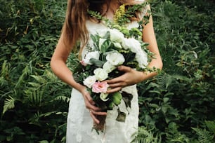 stylish rustic bouquet in the hand of gorgeous boho bride on the background of grass and mountains
