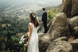 élégant magnifique couple de jeunes mariés debout sur les rochers dans les montagnes dans la lumière du soir