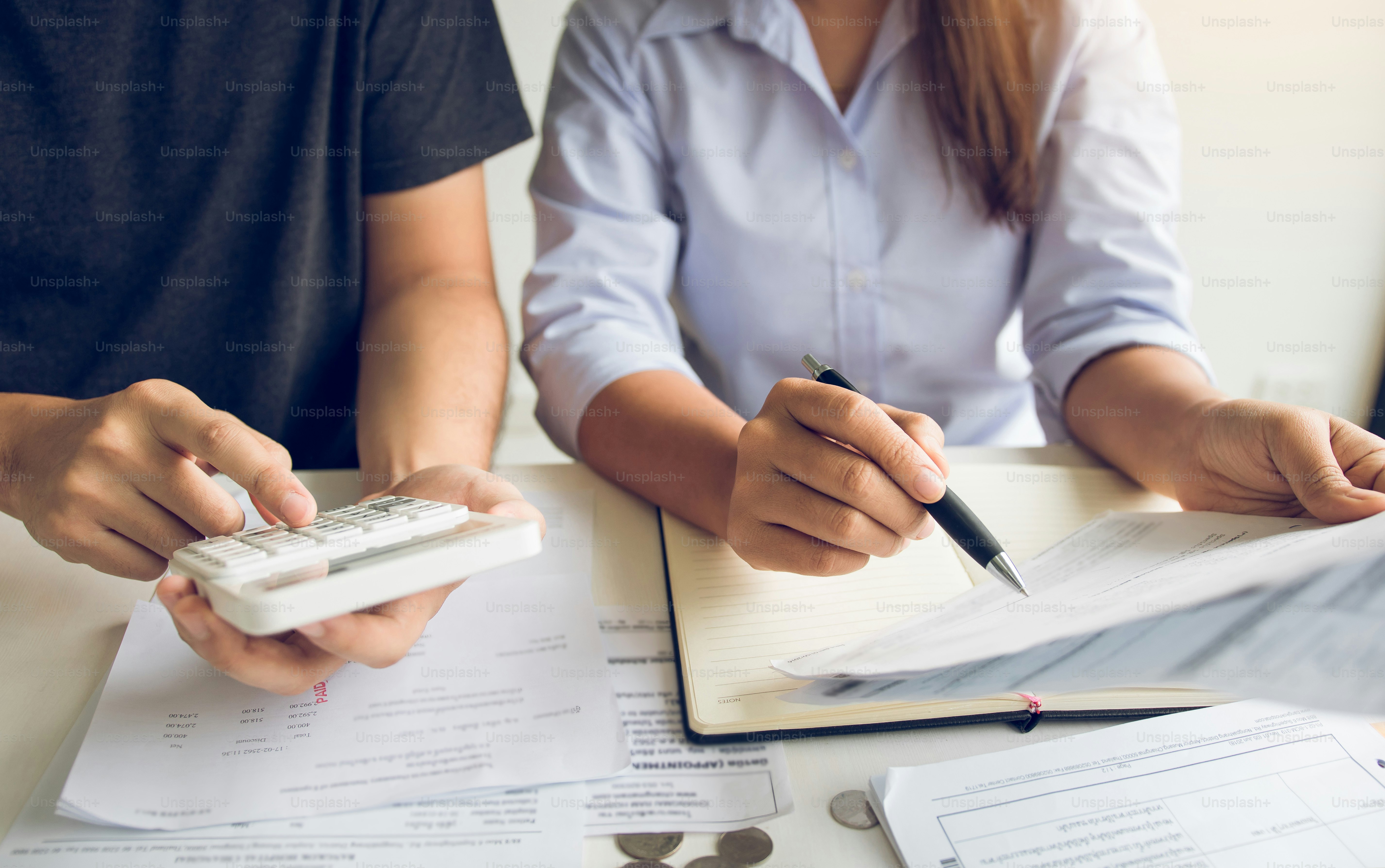 Two people reviewing financial documents with a calculator and pen at a desk