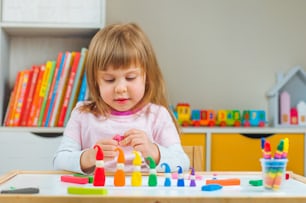 子供部屋のテーブルの上で子供の遊びの粘土からカラフルなノームを成形する小さな女の子。家族のためのホームアクティビティ。