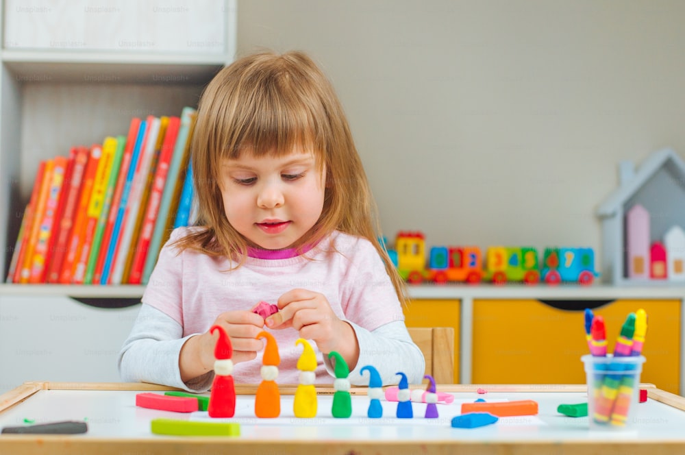 어린 소녀는 아이 방의 테이블에 있는 어린이 놀이 점토에서 다채로운 격언을 성형합니다. 가족을위한 가정 활동.
