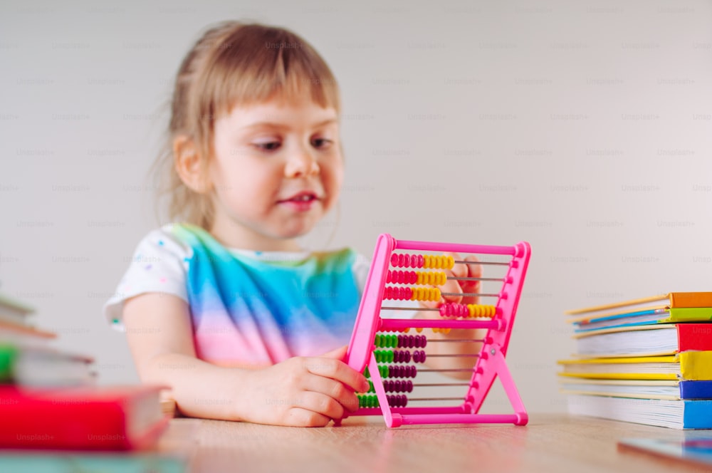 Beautiful little girl playing with colorful plastic abacus toy sitting at the table. Selective focus on the abacus.