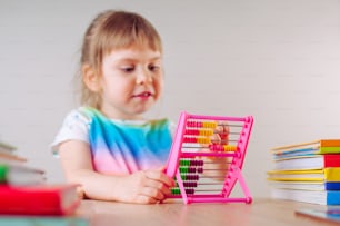 Hermosa niña jugando con colorido juguete de ábaco de plástico sentada en la mesa. Enfoque selectivo en el ábaco.