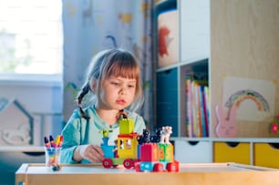 Niña jugando con el tren de juguete de plástico de los niños con coloridos cubos de números en la habitación de los niños. Actividades en casa para niños.