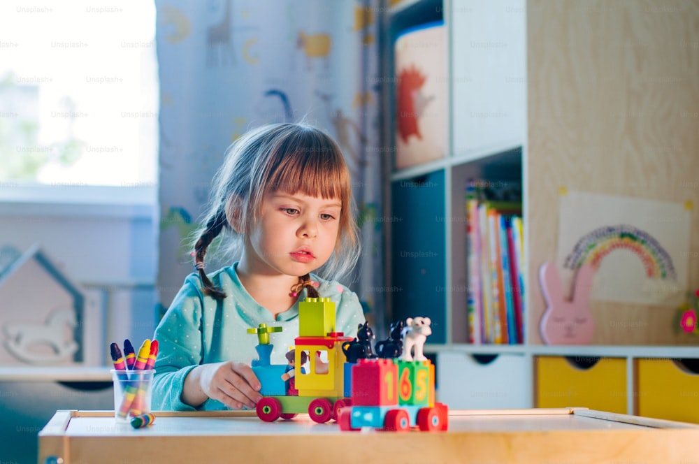 Little girl playing with kids plastic toy train with colorful number cubes in the kids room. Home activities for kids.