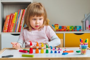 Little girl molding colorful gnomes from child's play clay on the table in the kids room. Home activities for family."n