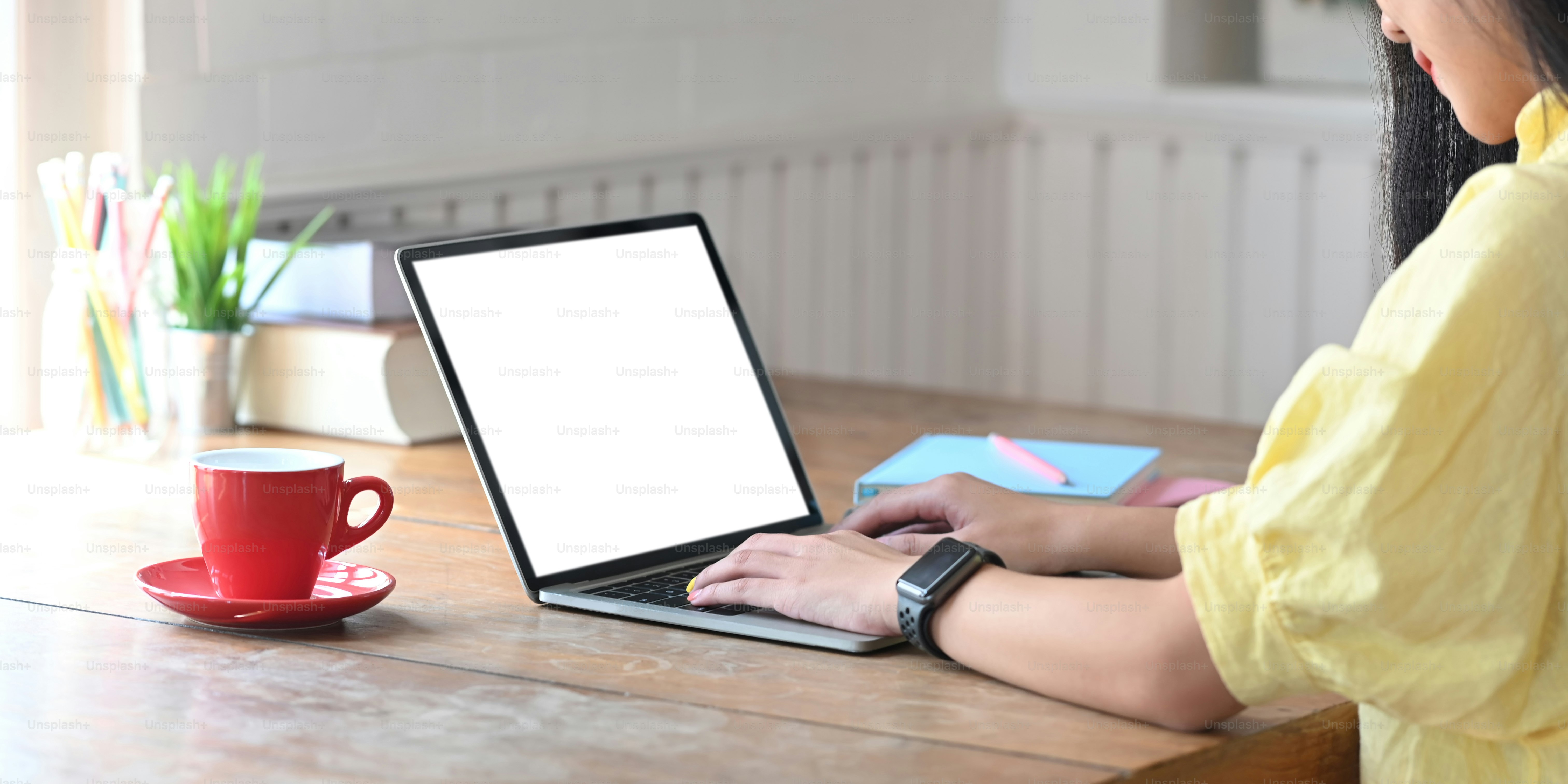 Mujer elegante de primer plano que escribe en la computadora portátil con pantalla blanca en blanco mientras está sentada en el escritorio de trabajo de madera sobre la cómoda sala de estar como fondo.