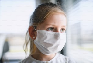 Vista frontal de una niña pequeña con máscaras faciales en el interior de la casa, virus Corona y concepto de cuarentena.