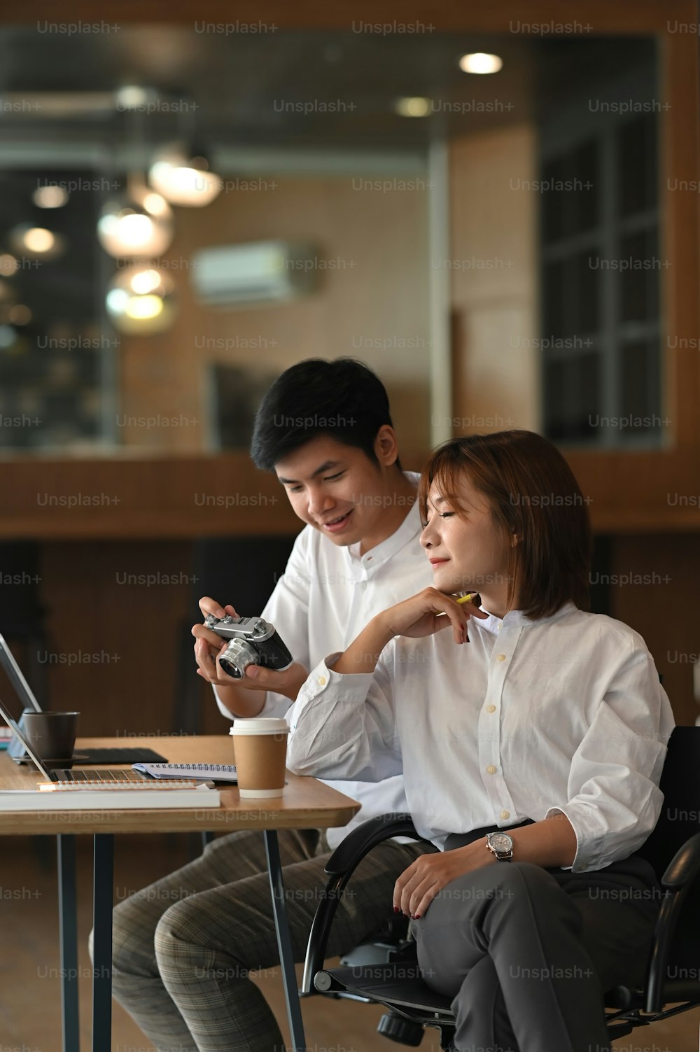Photo of young couple working together with computer laptop and document while sitting at the wooden working desk over comfortable cafe as background.