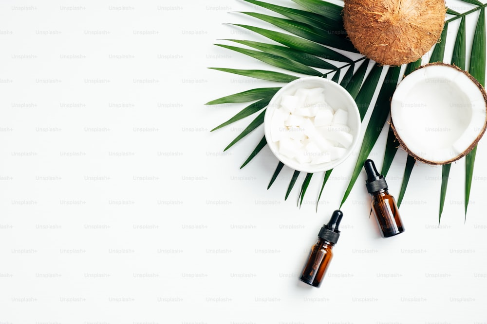 Coconut oil for hair with tropical palm leaf on white background. Flat lay, top view, copy space. Natural organic cosmetic for hair treatment concept