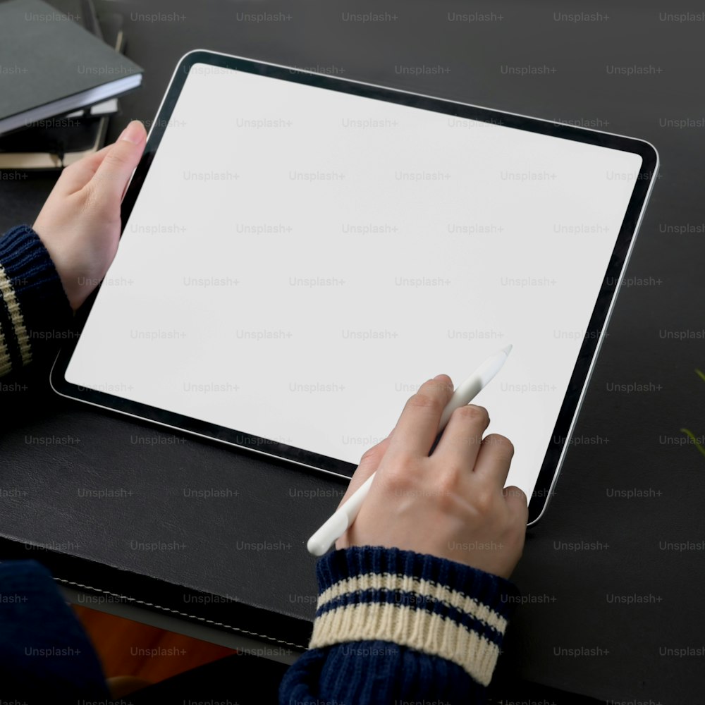 Plan recadré d’une pigiste travaillant sur une tablette à écran vide avec un stylet à une table de travail moderne sombre
