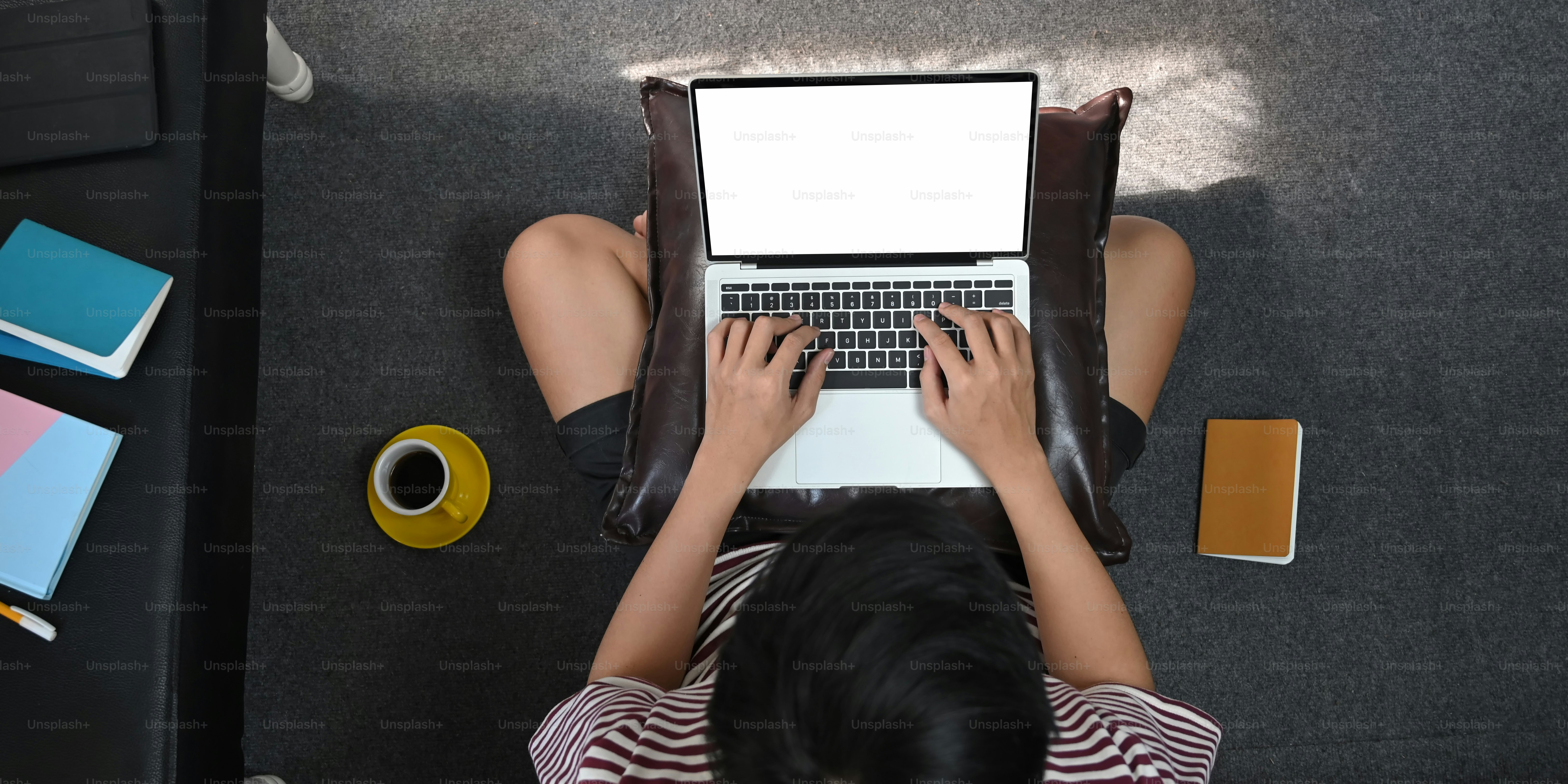 Gambar tampilan atas pria kreatif mengetik di laptop komputer layar kosong putih yang meletakkan pangkuannya sambil duduk di lantai di ruang tamu yang nyaman. Konsep bekerja dari rumah.