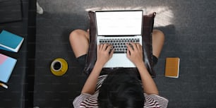 Imagen de la vista superior del hombre creativo que escribe en la computadora portátil de la pantalla blanca en blanco que se pone en su regazo mientras está sentado en el suelo en la cómoda sala de estar. Concepto de trabajo desde casa.