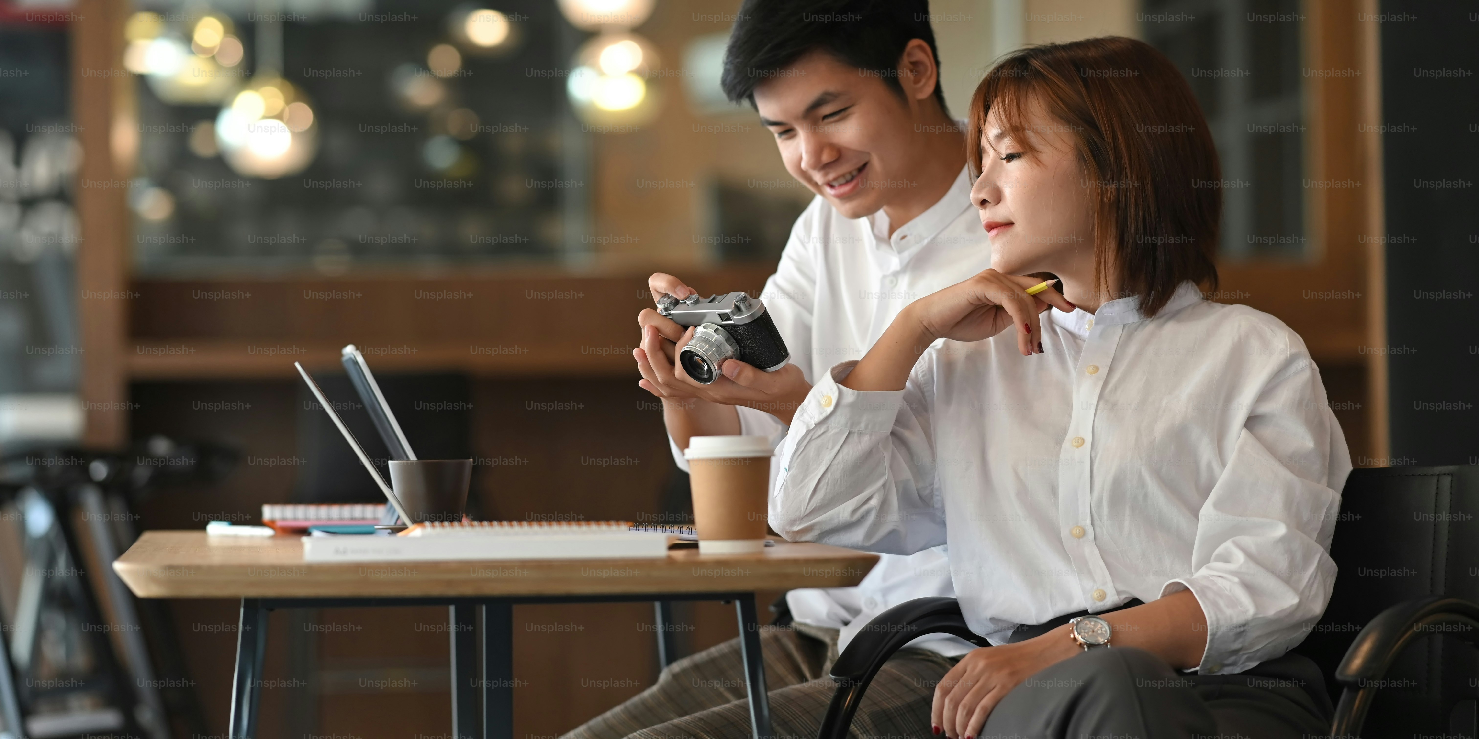 Photo of young couple working together with computer laptop and document while sitting at the wooden working desk over comfortable cafe as background.