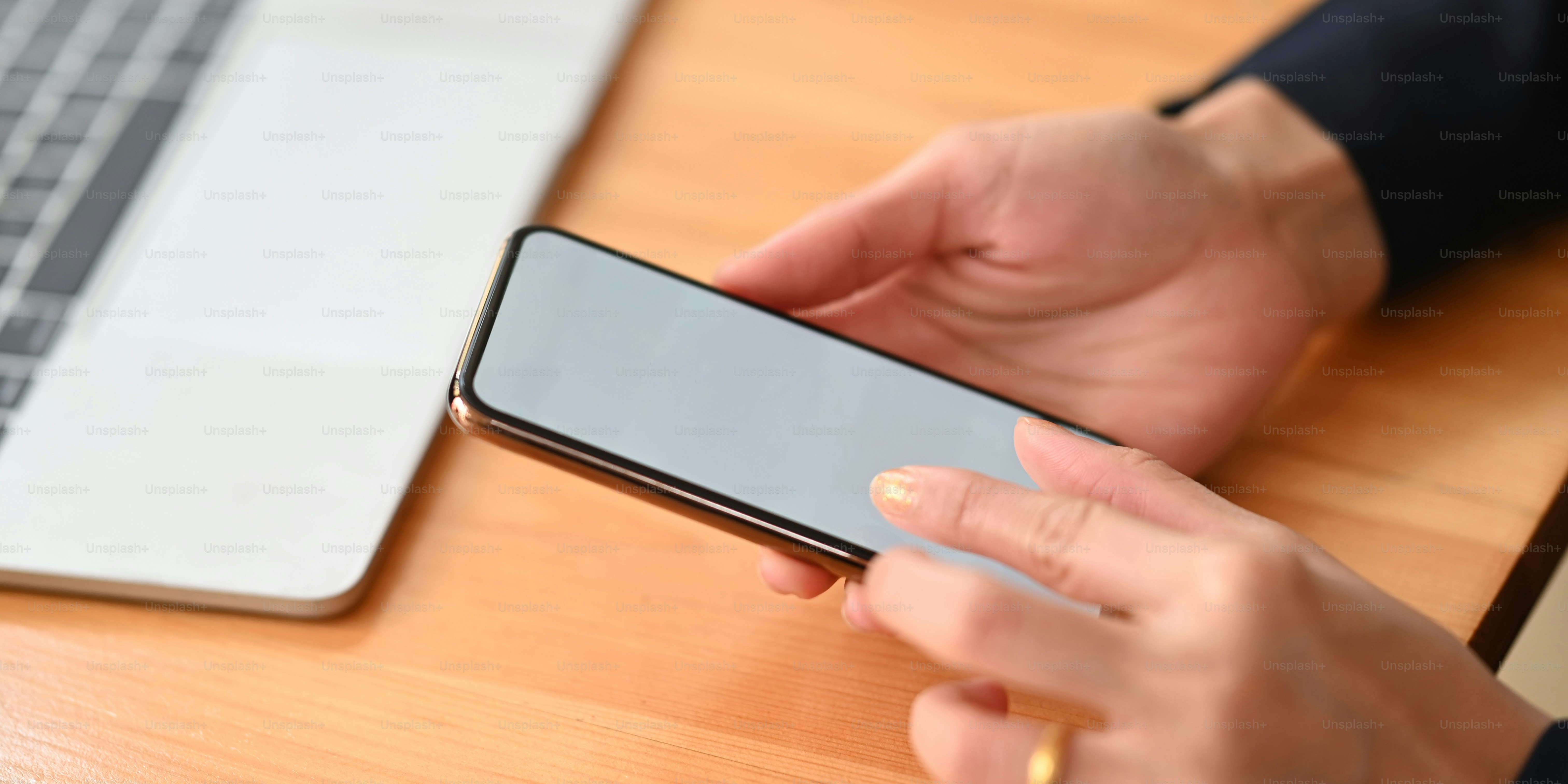 Closeup woman's hands holding and using a smartphone while sitting/relaxing at the wooden working desk over comfortable living room as background.