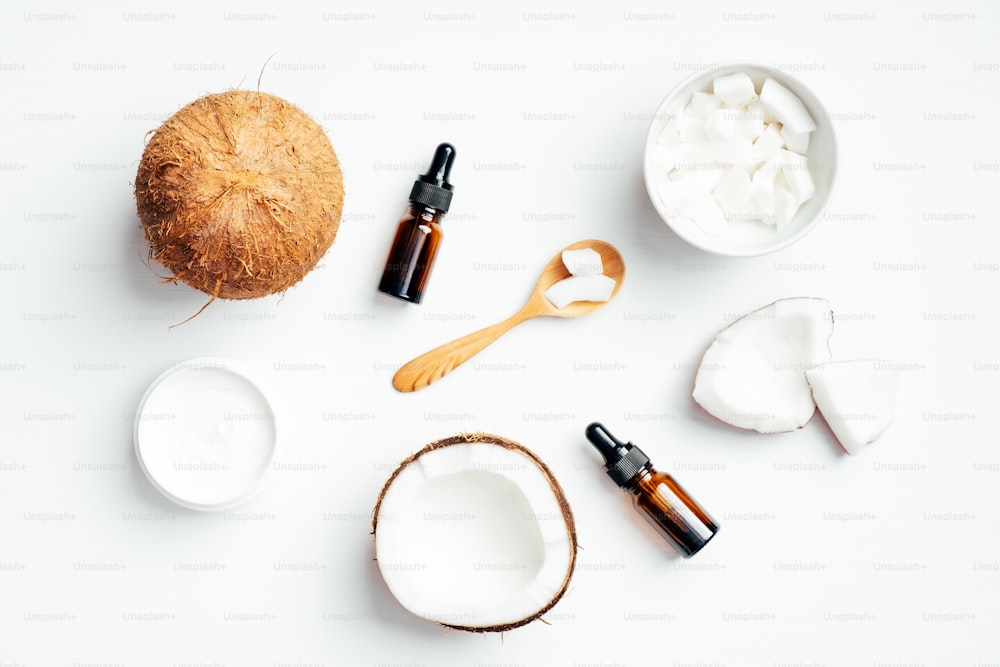 ボディケア用の天然有機ココナッツ化粧品を使用したフラットレイ組成物。白い背景にココナッツ、エッセンシャルオイル、保湿クリームの上面図。スキンケア、SPAマッサージのコンセプト