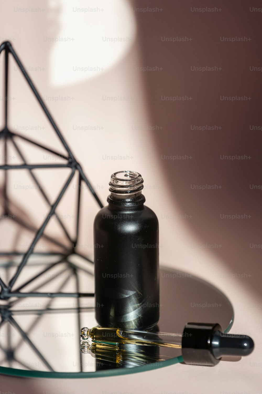 Vista verticale della bottiglia di vetro nera con olio antietà facciale in pipetta in piedi sullo specchio su sfondo rosa pastello con spazio di copia