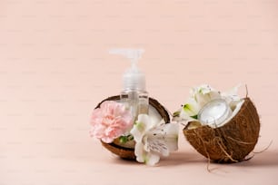 Plastikflaschen mit Spender in der Nähe von Blumen, Kokosölkörper oder Gesichtscreme isoliert auf pastellrosa Hintergrund mit Kopierraum. Konzept eines tropischen, exotischen und natürlichen Biokosmetikprodukts