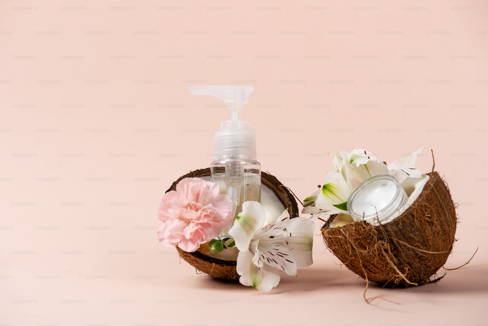 Plastic bottles with dispenser near flowers, coconut oil body or face cream isolated on pastel pink background with copy space. Concept of tropical, exotic and natural organic cosmetics product