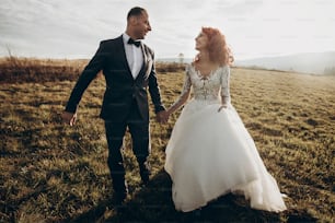happy wedding couple walking in sunlight, holding hands in mountains at sunset light. gorgeous boho newlyweds, stylish bride and groom, true feelings. emotional romantic moment. space for text