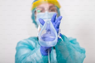 Arzt hält Sauerstoffmaske hoch, als wolle er Patient im Krankenhaus anlegen, Mitarbeiter des Gesundheitswesens in der Coronavirus-Covid19-Pandemie in Schutzausrüstung setzen Sauerstoffmaske auf Patientendiagnose des Coronavirus