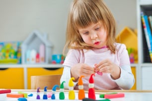 Petite fille moulant des gnomes colorés à partir d’argile de jeu d’enfant sur la table de la chambre des enfants. Activités à domicile pour la famille.