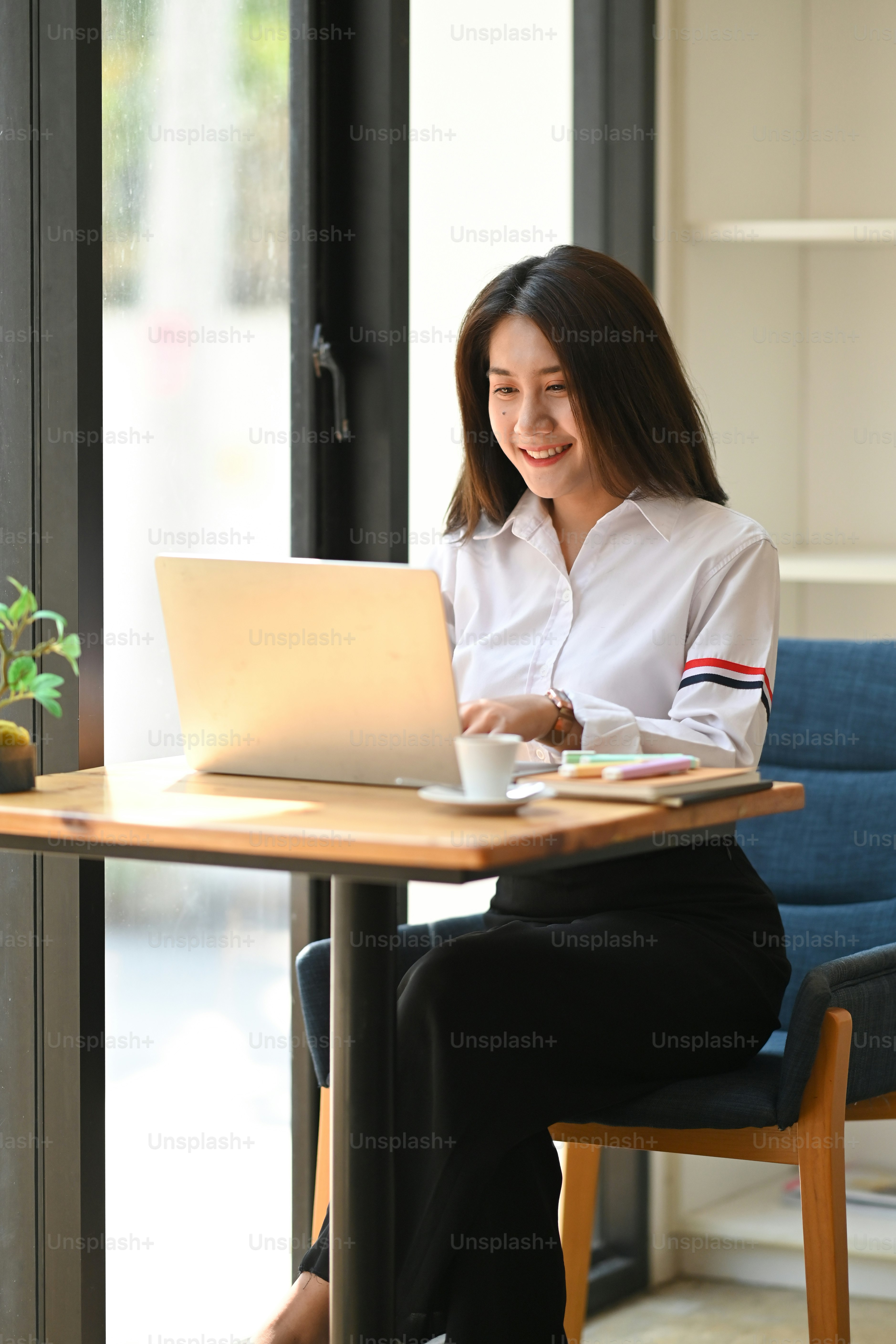 Photo of gorgeous woman working as accountant typing on computer laptop while sitting at the wooden working desk over comfortable cafe book shelf as background.