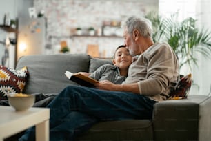 Grandpa and grandson reading book together. Grandfather and grandson enjoying at home.