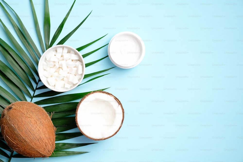 Crema cosmética de coco con hoja de palma y rodajas de coco sobre fondo azul. Plano, vista superior. Producto de belleza orgánico natural SPA para el cuidado de la piel de las manos, tratamiento corporal