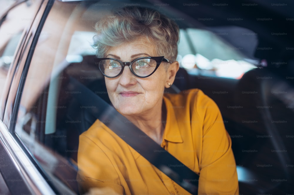 차에 앉아 안경을 쓴 매력적인 노인 여성. 유리를 통해 촬영했습니다.