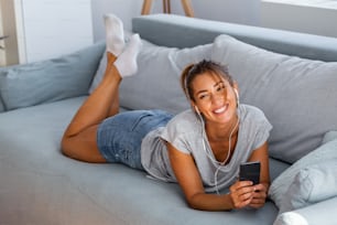 Happy young woman in earphones is listening to music with smart phone, dancing and smiling. Young woman listening to music online on smartphone in headphones