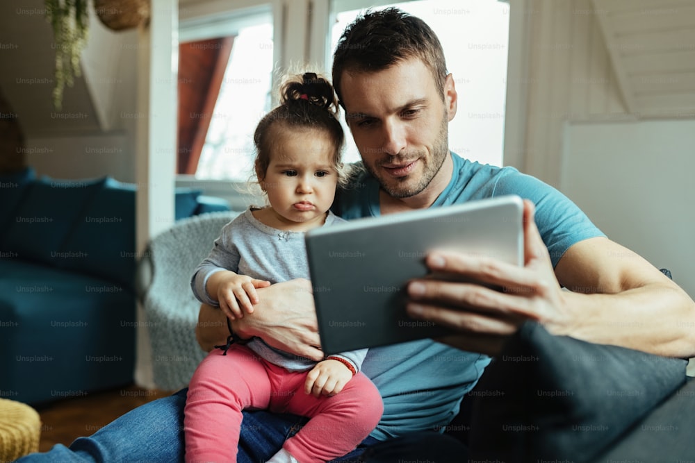 Young father using touchpad with his small daughter while relaxing at home.