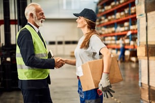 Poignée de main heureuse d’une employée d’entrepôt avec le directeur de l’entreprise dans un compartiment de stockage industriel.