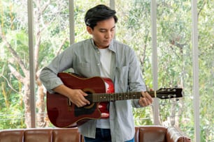 Young guitar player holding his guitar at home. Music and song concept.